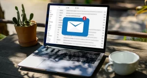 Ein Laptop steht auf einem Holztisch, auf dem Bildschirm des Laptops ist eine Benachrichtigung zu sehen, welche darauf hinweist, dass eine neue E-Mail eingetroffen ist.